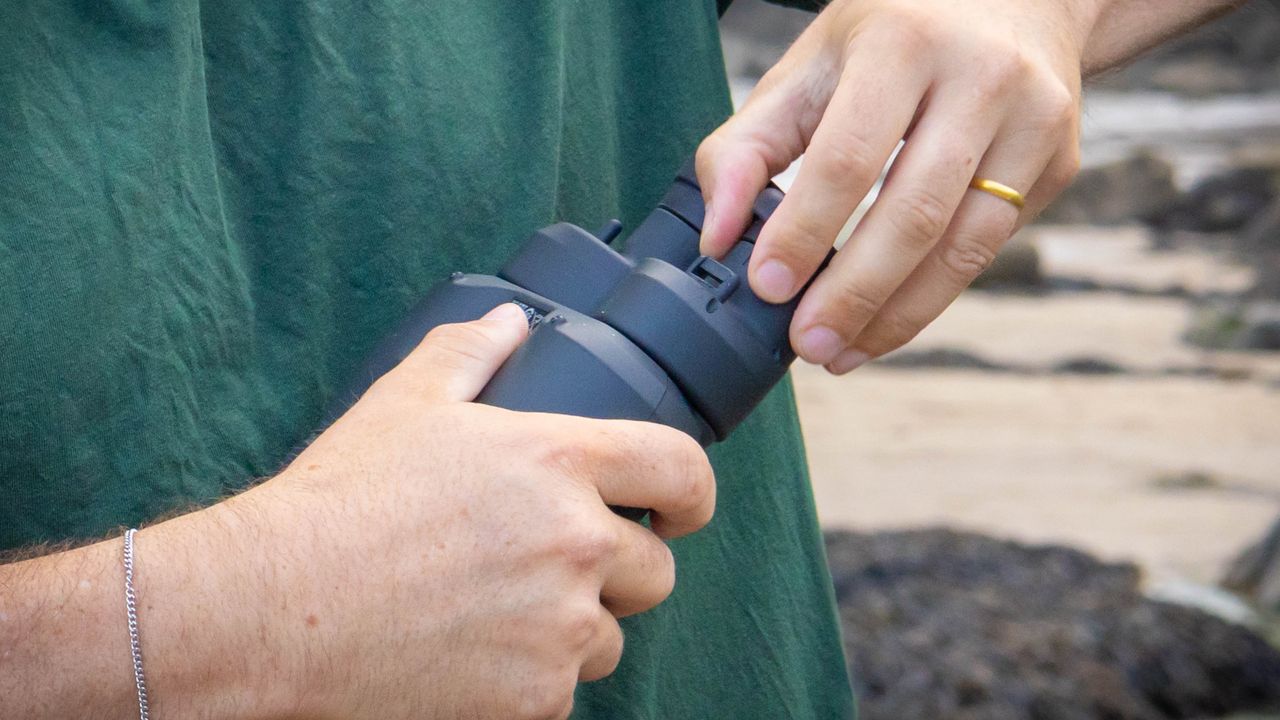A person demonstrating how to adjust the eyecups on the Canon 12x36 IS III binoculars.
