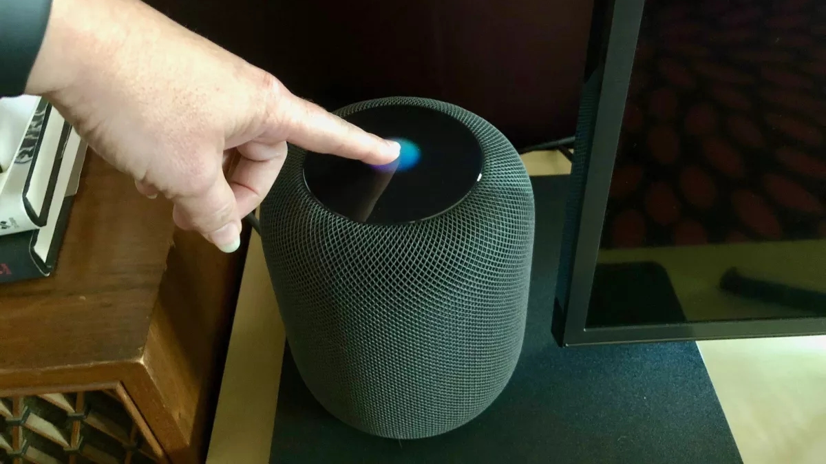 A person performing the reset procedure on a HomePod by holding a finger on the Touch Panel.