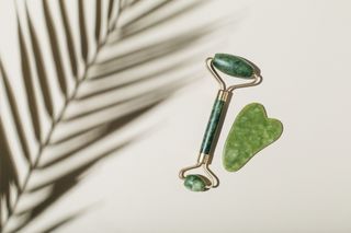 a jade roller and gua sha on a beige background with a fern leaf shadow