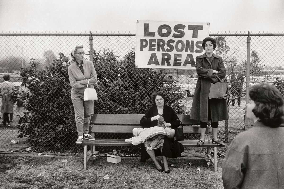 A black and white photo of women and a child in a 'Lost Persons Area' with a fence and bushes in the background