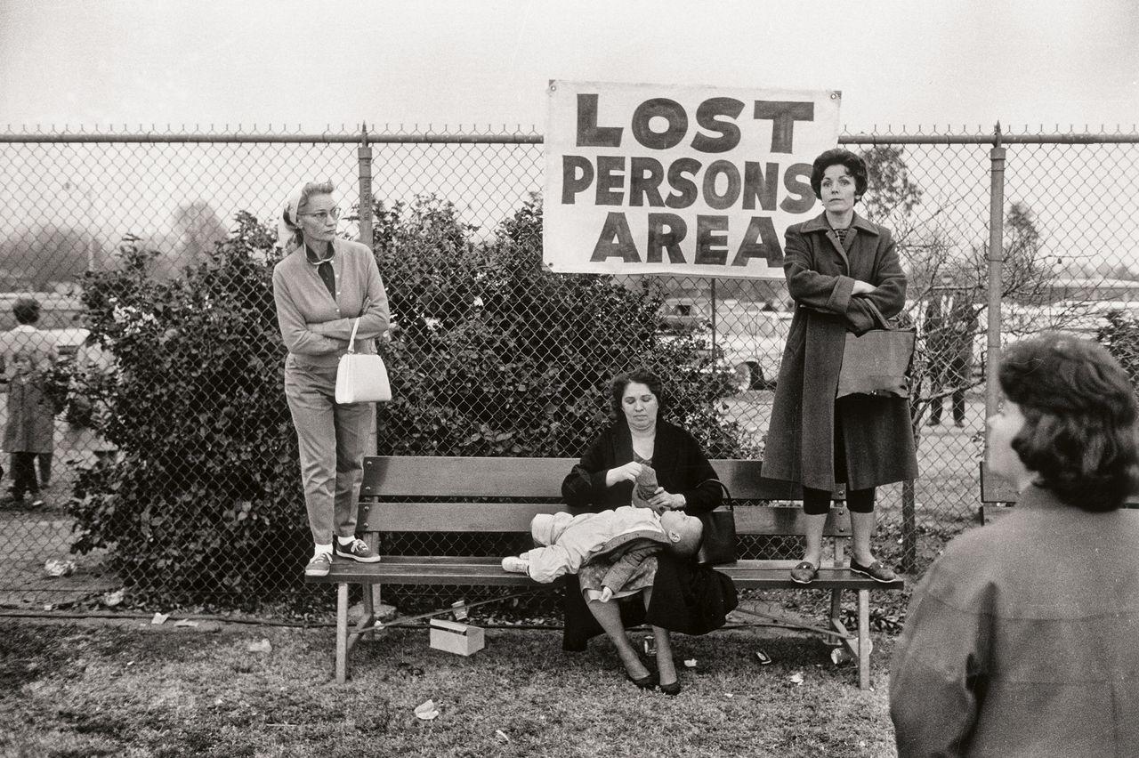 A black and white photo of women and a child in a 'Lost Persons Area' with a fence and bushes in the background