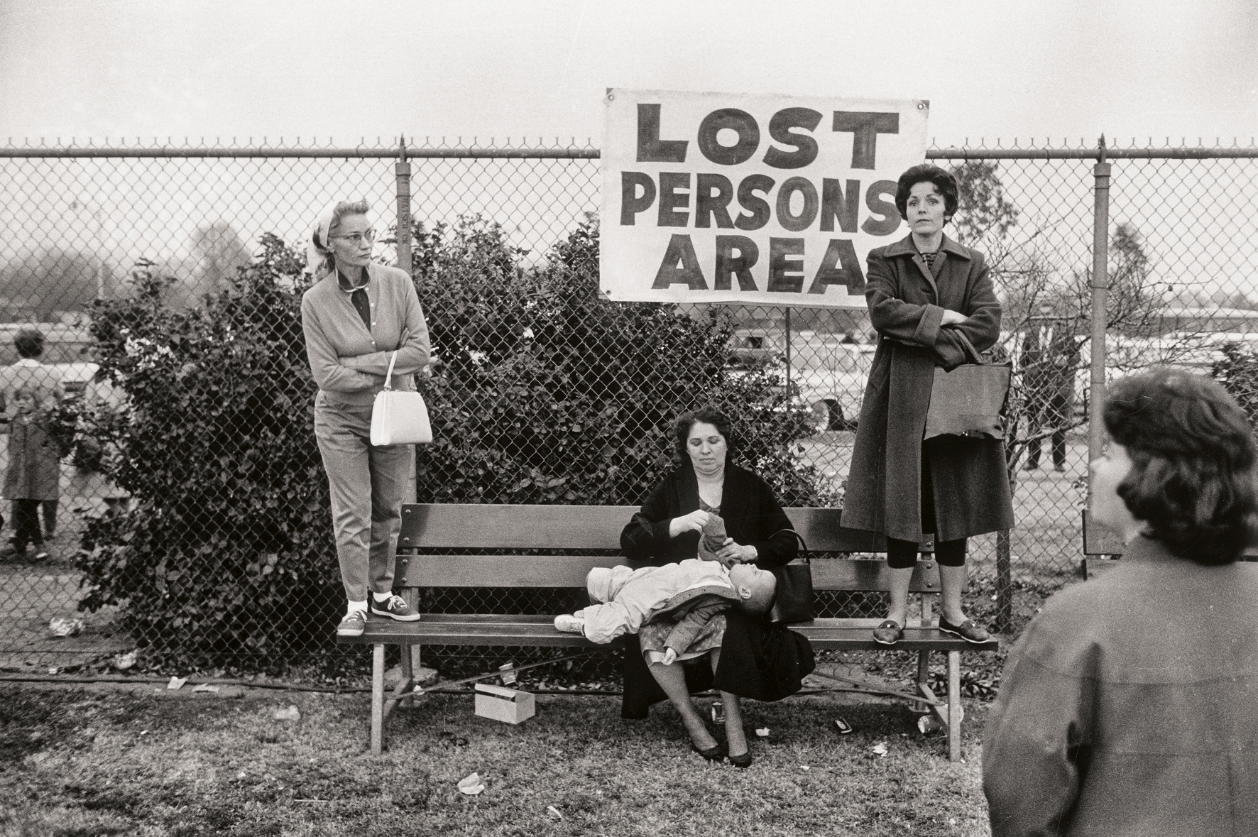 A black and white photo of women and a child in a 'Lost Persons Area' with a fence and bushes in the background