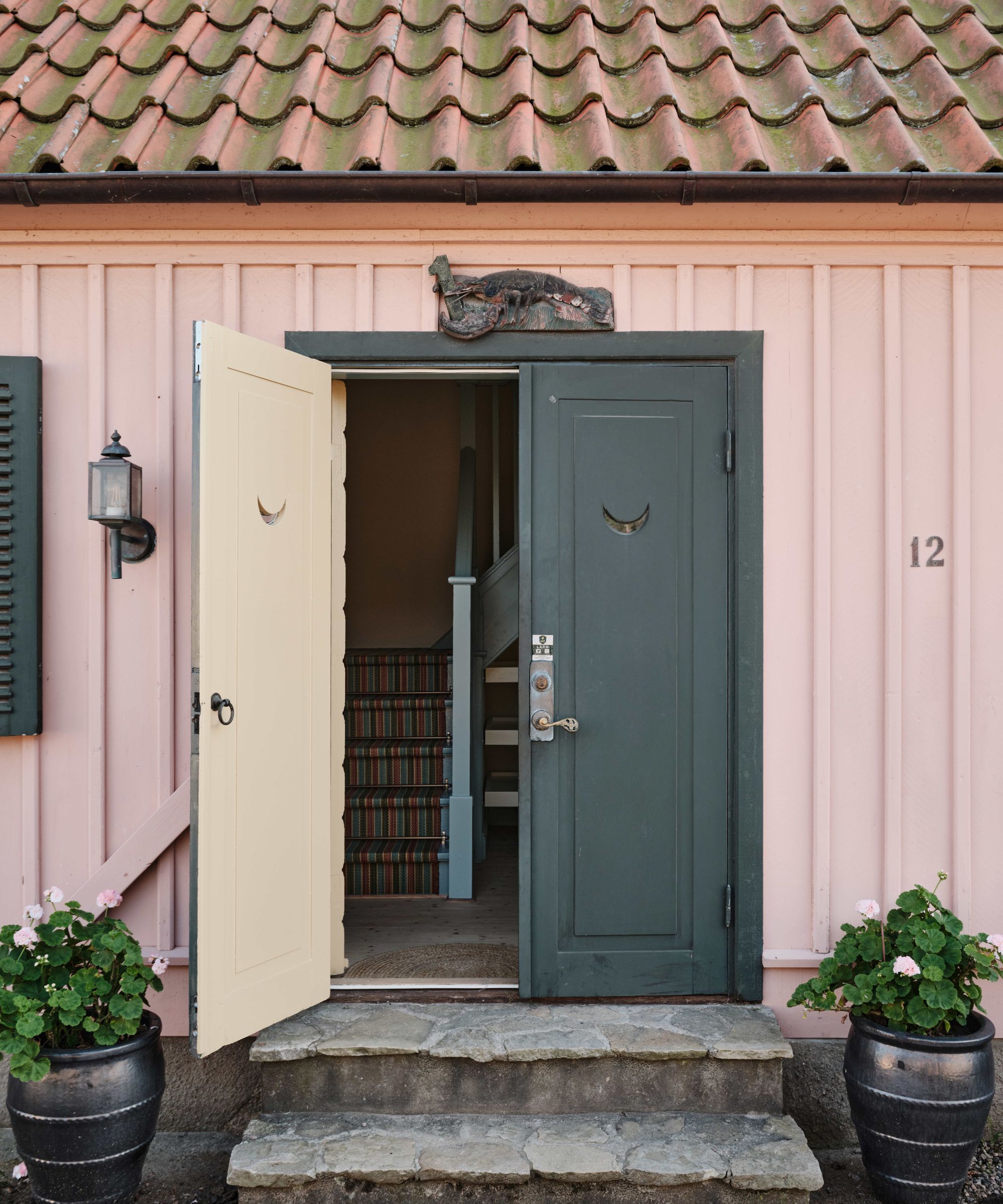 Exterior of a rustic Swedish summer house with pink walls and a dark gray double front door