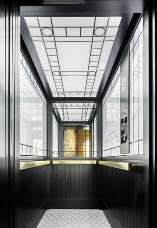 The inside of an elevator with black sides, glass windows and a patterned floor.