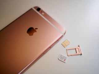 A couple SIM cards lay next to a rose gold iPhone