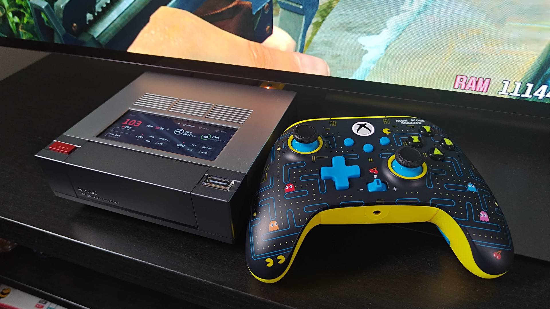 PowerA Pac-Man controller next to Ayaneo Mini PC on black TV bench.