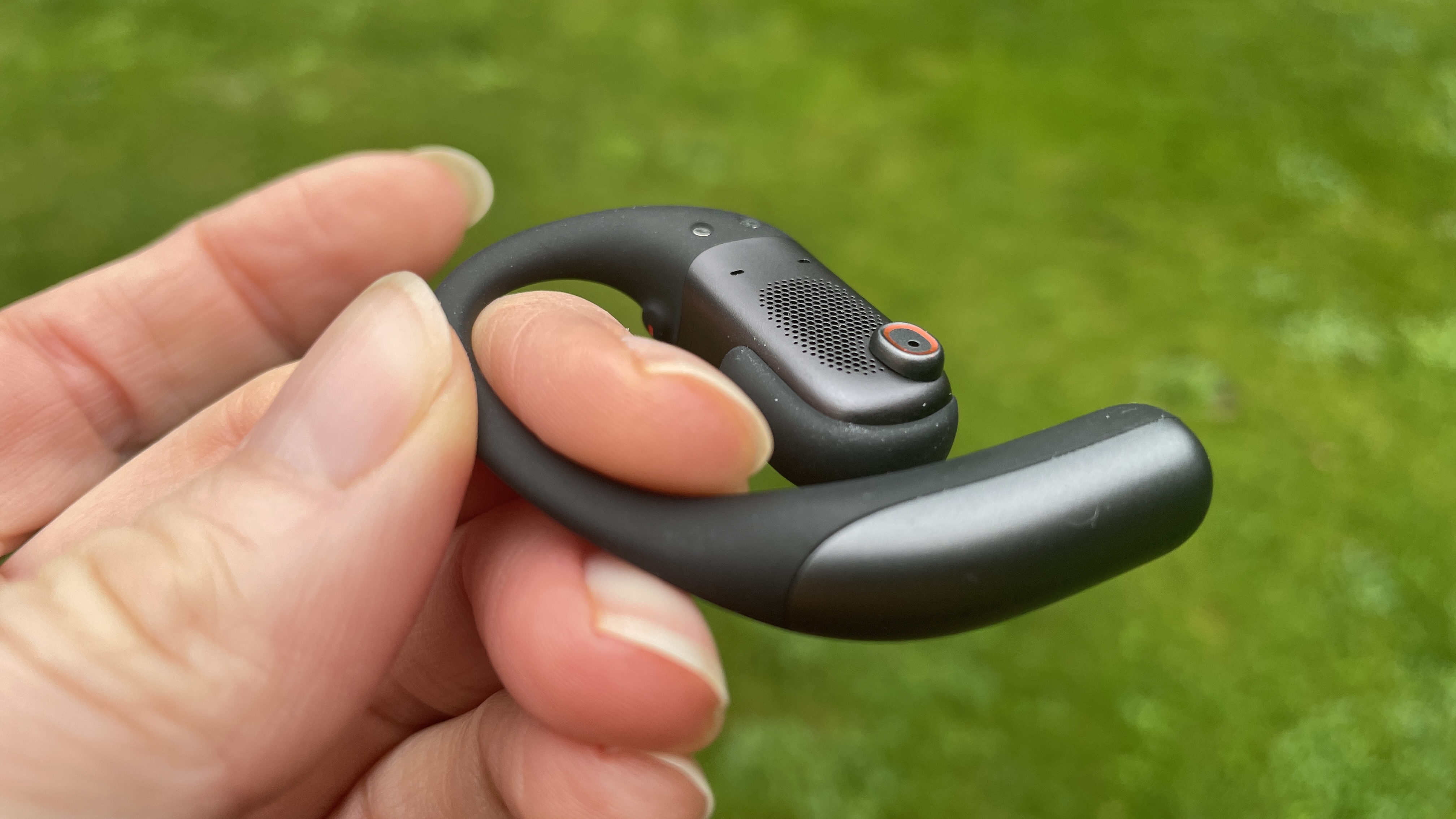 Shokz Openfit Pro outside, outside held in a woman's hand, with green grass in the background