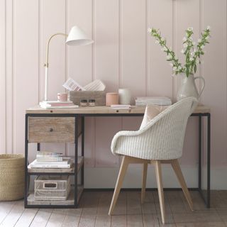 Desk and chair in front of a panelled wall painted pale pink, a basket drawer and storage.