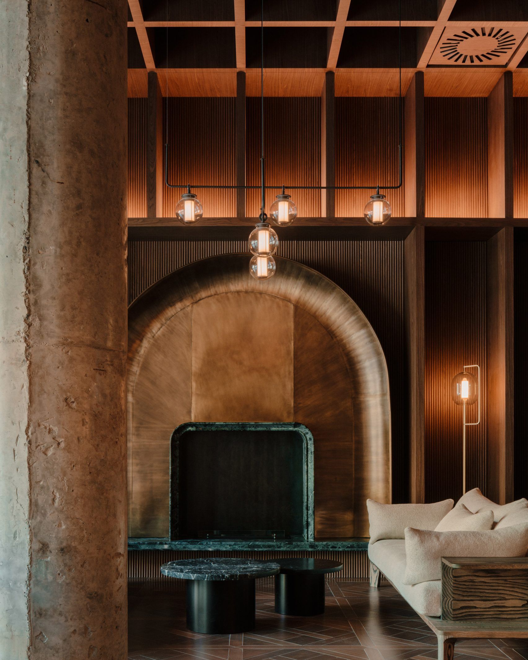 The brutalist-warm interiors of a luxury hotel sitting inside a former Soviet-era office feature checkered black and white, or wooden, floors, spherical soft lighting, and wooden furniture throughout.