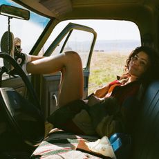 zendaya as rue laying in the passenger seat of an old looking guitar with the door open as it sits in the desert in a still from euphoria season 3