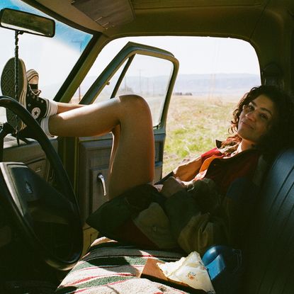 zendaya as rue laying in the passenger seat of an old looking guitar with the door open as it sits in the desert in a still from euphoria season 3