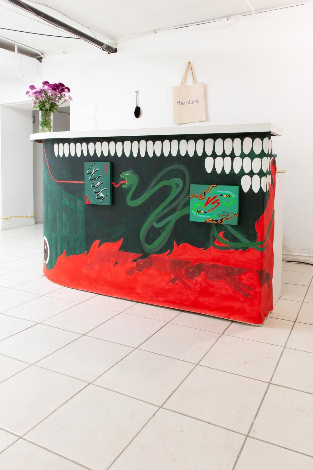 A gallery bar redecorated to look like an artwork in its own right through abstract compositions in green, red, and black, located next to a bookcase stakced with volumes.