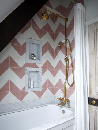 small bathroom with built in bath with gold brassware and pink and white chevron tiles on the wall