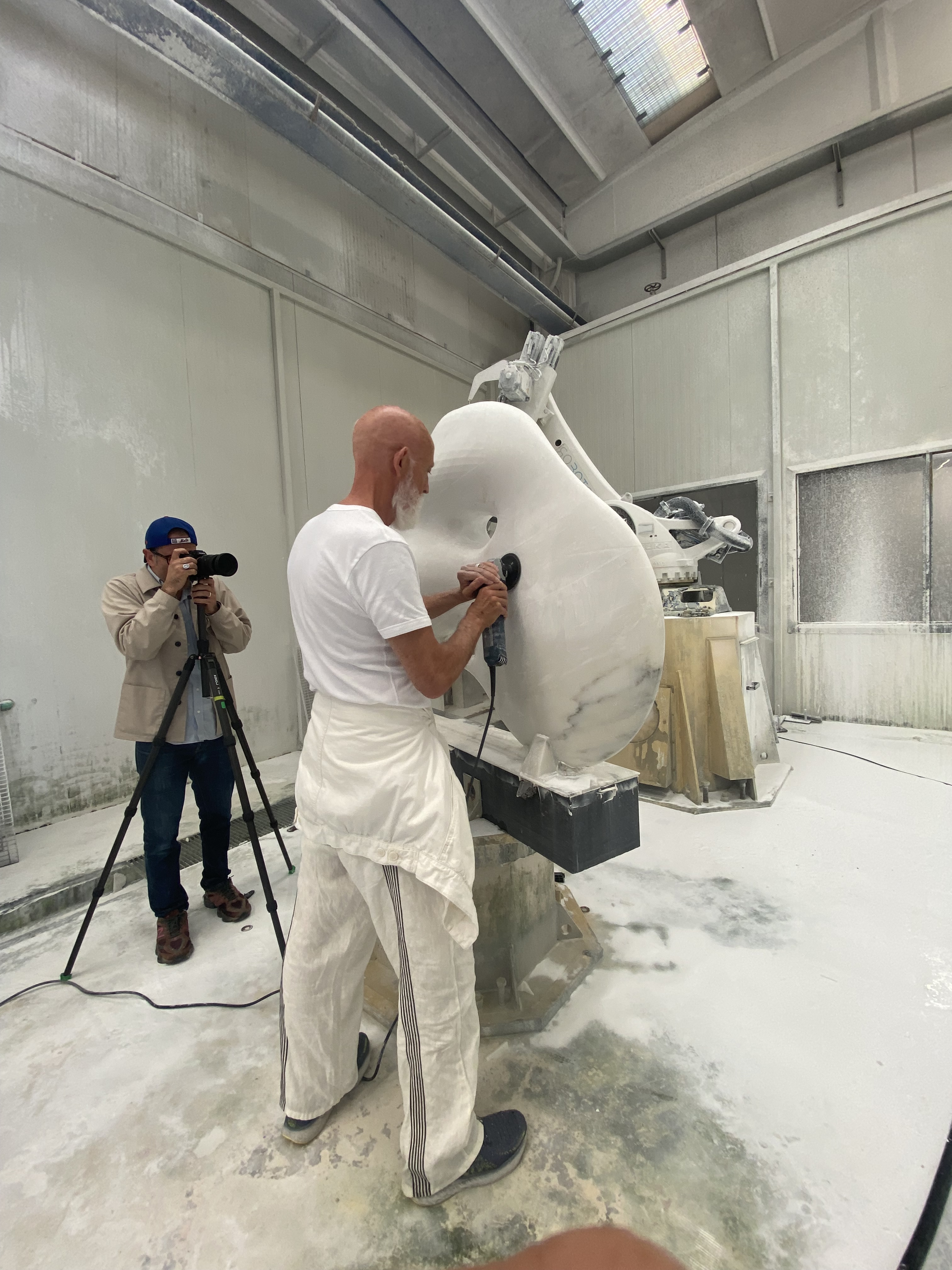 Man dressed in white carving marble sculpture in a workshop setting