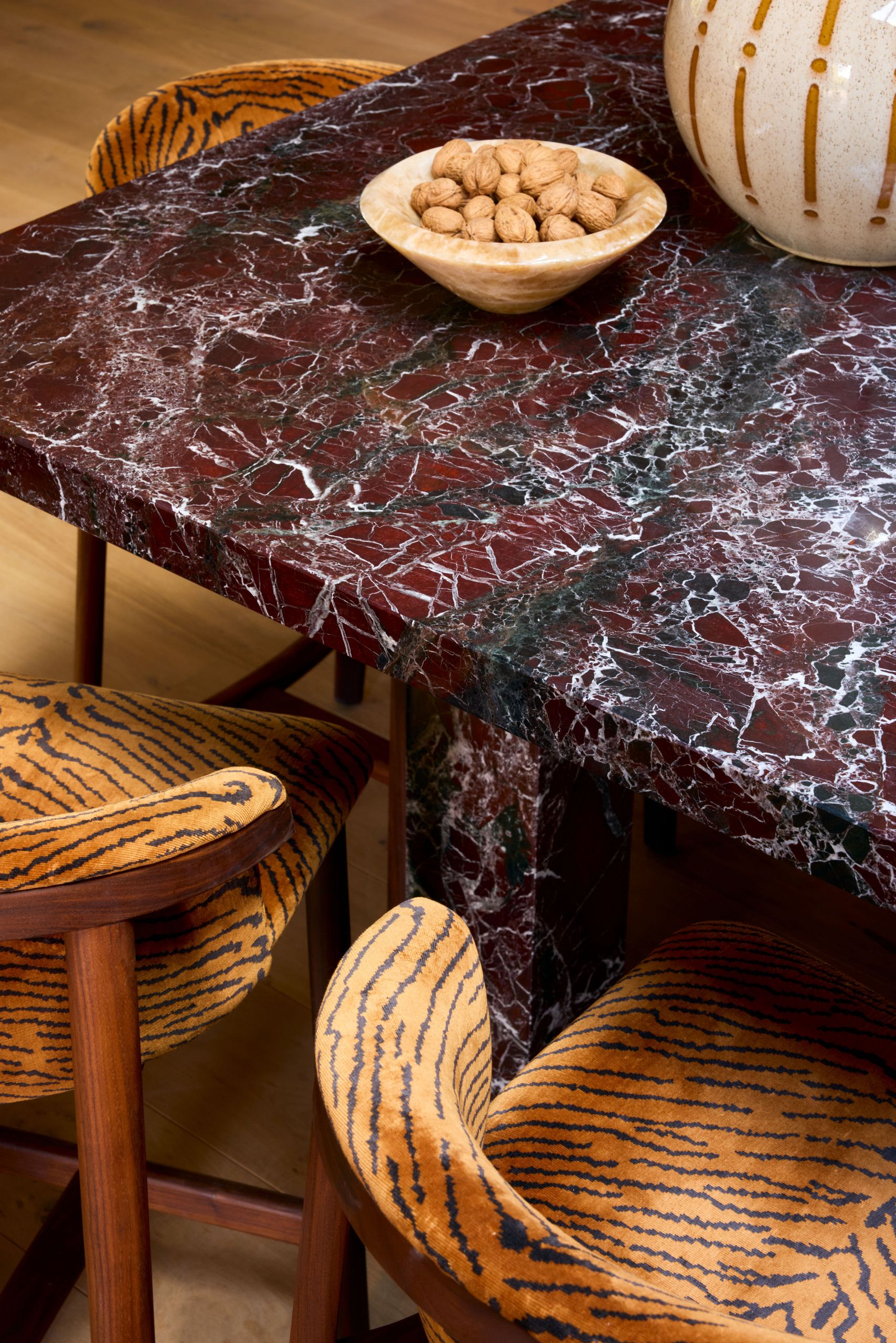 Close-up of a red marble kitchen island with a bowl of nuts on it and three orange tiger print bar chairs around it.