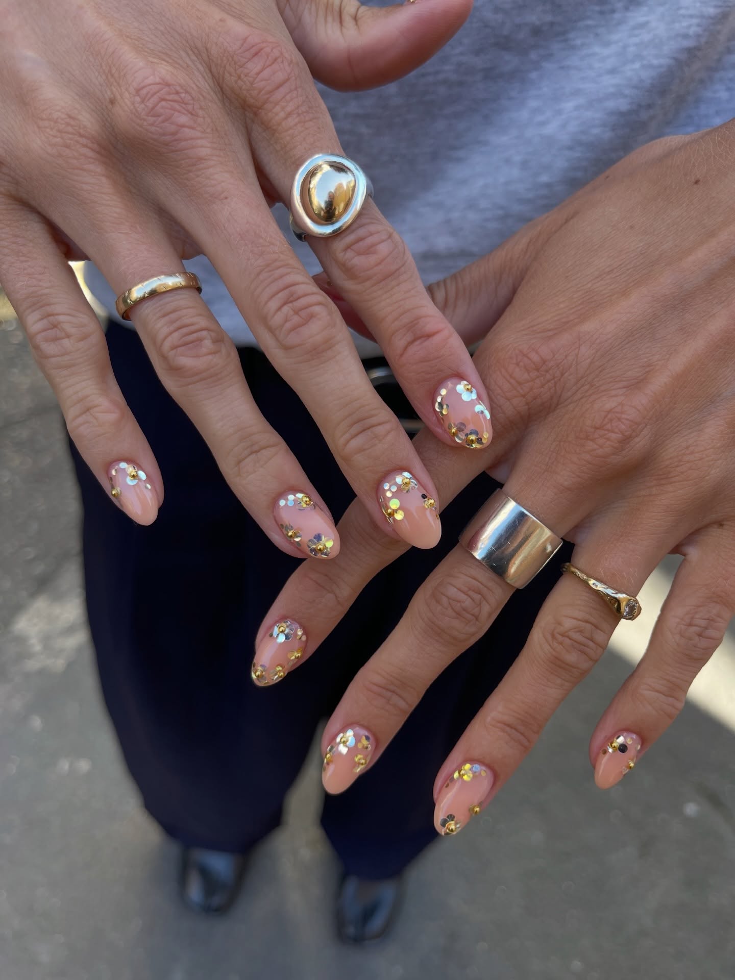 sheer nude almond nails decorated with tiny silver and gold sequins arranged into delicate floral clusters across each nail