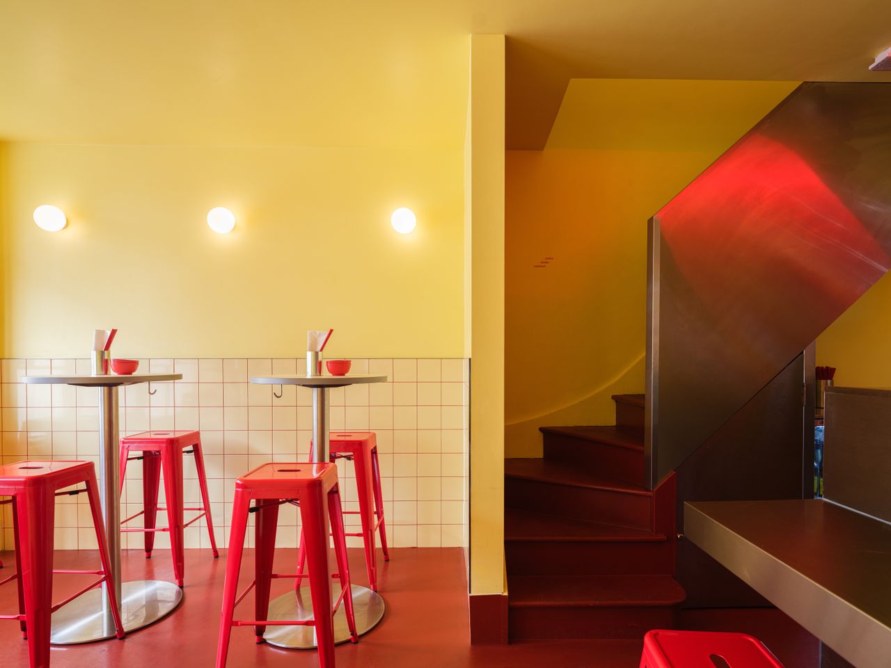 An inventively designed, small eatery features buttery brick walls, red floors and furniture mixed with chrome decor, and spherical, softly glowing opaque glass sconces.