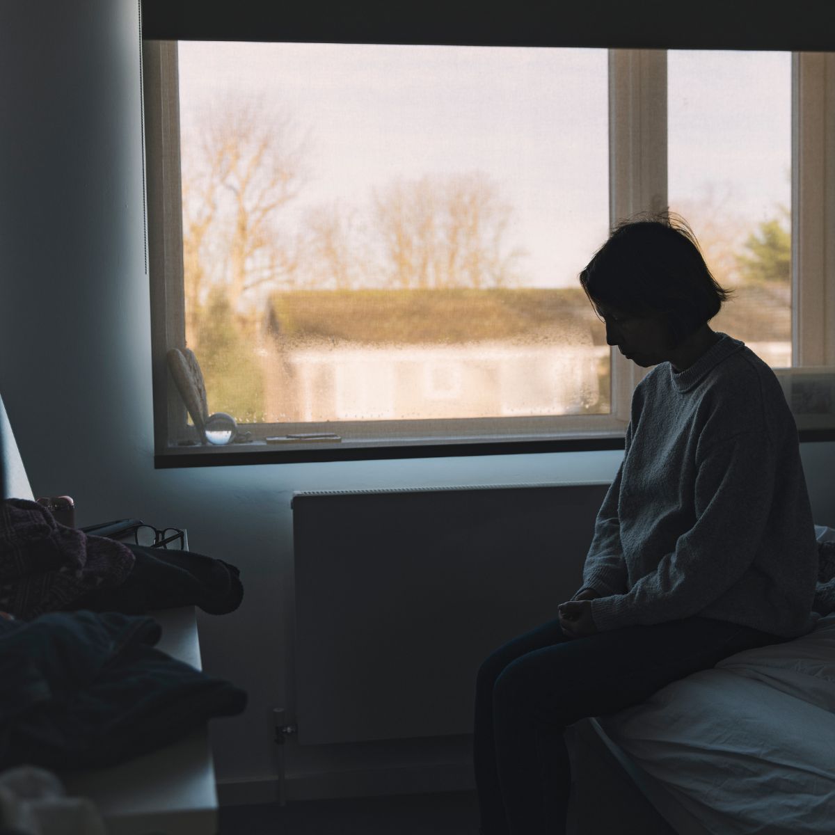 Side view of a woman sitting in her bedroom - negative emotion - stock photo
