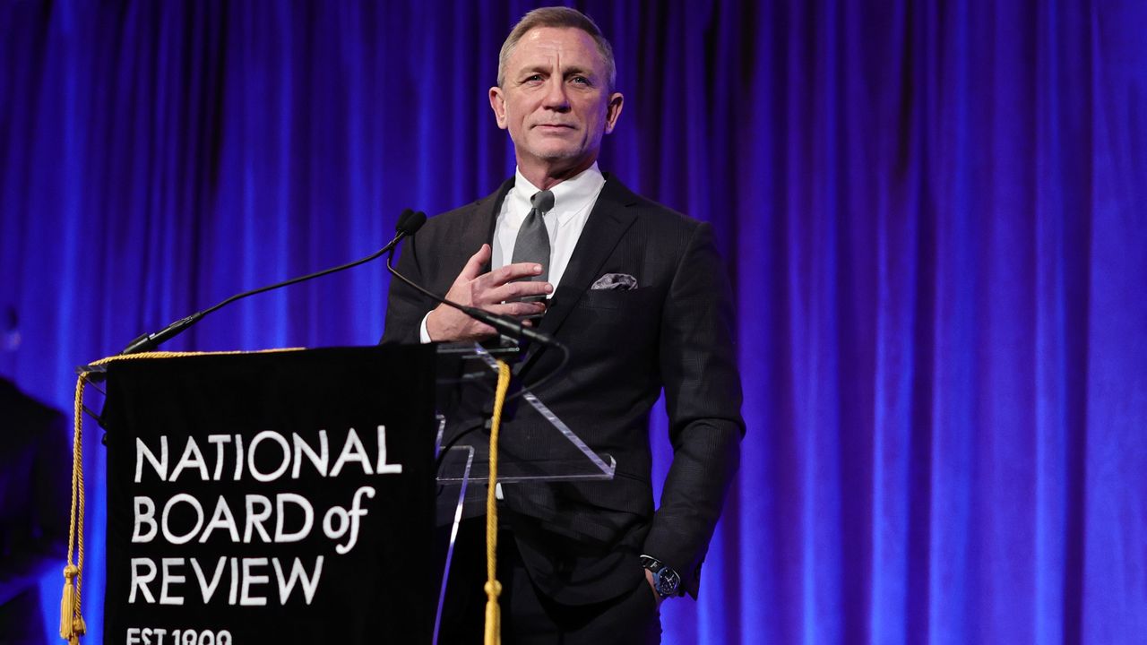 Daniel Craig in front of blue curtain wearing a MoonSwatch