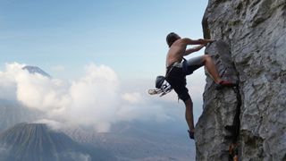 photo of a man rock climbing with mountains pictured in the background