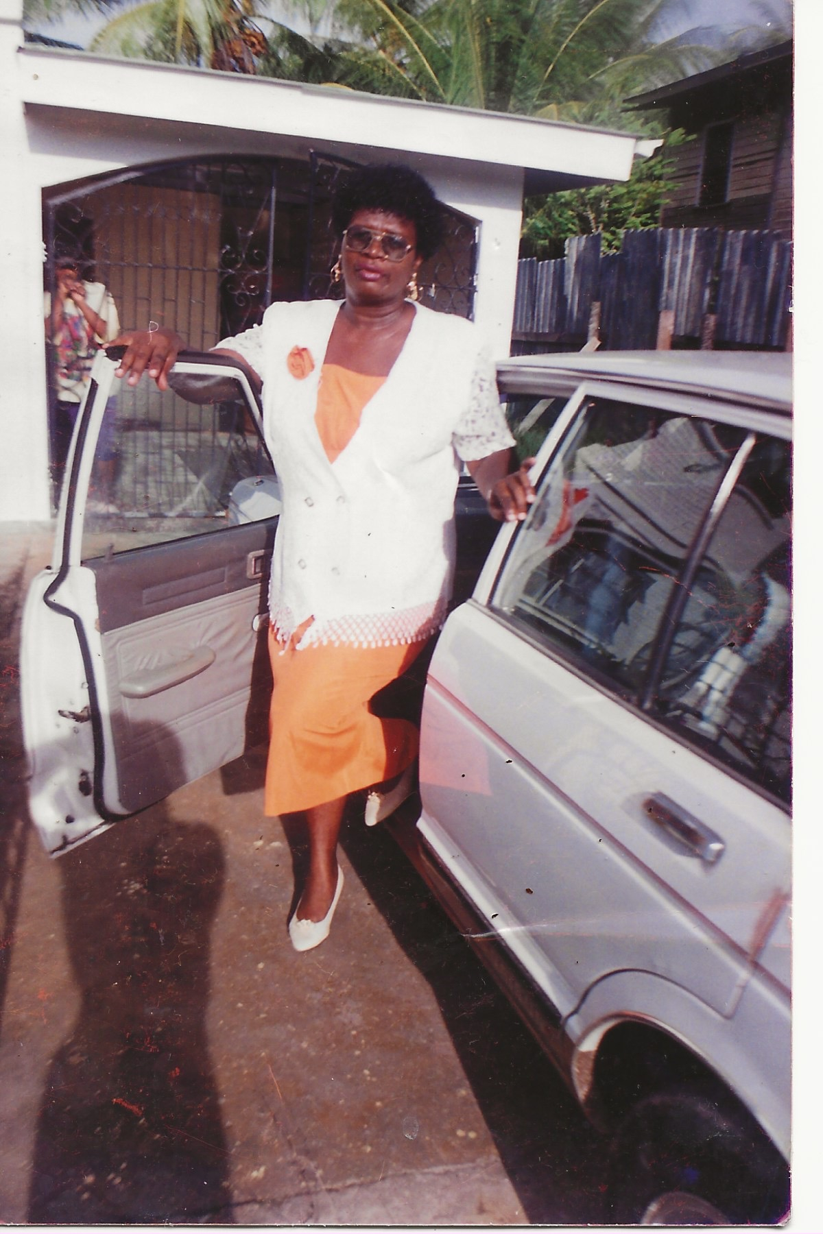 A woman in a yellow dress and white jacket wearing gold jewelry