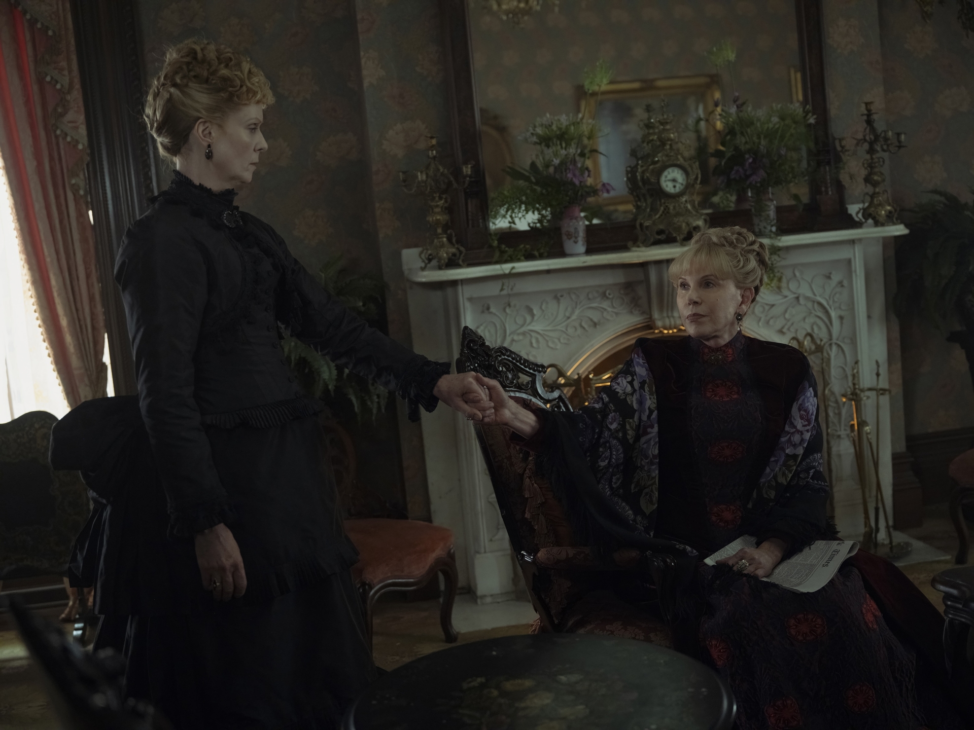 cynthia nixon standing and holding hands with christine baranski sitting in a parlor in the gilded age season 3