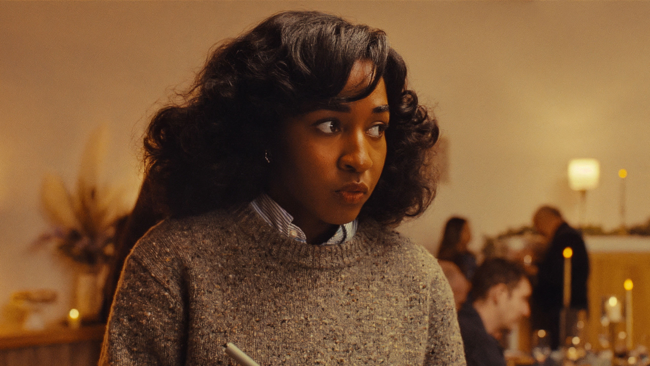 ayo edebiri wears a grey sweater and looks nervous at a dinner party in a still from opus