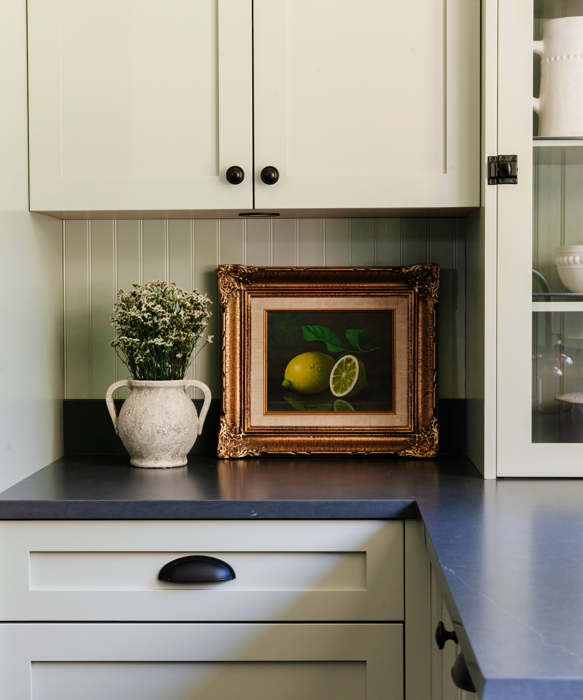 A sage green kitchen with black countertops and a gold frame