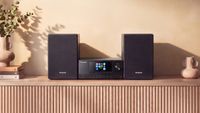 The Panasonic SC-PMX112 hi-fi system on a side unit next to a vase that sits on top of a stack of books.