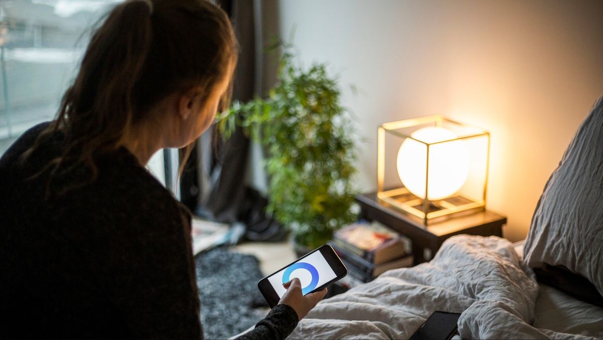 A woman sat on her bed using an app to adjust her smart mattress