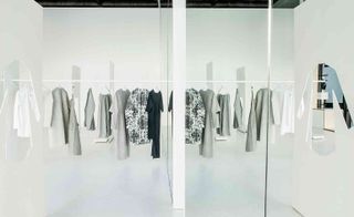 Hanging on long racks, the clothing echoes across two parallel rooms
