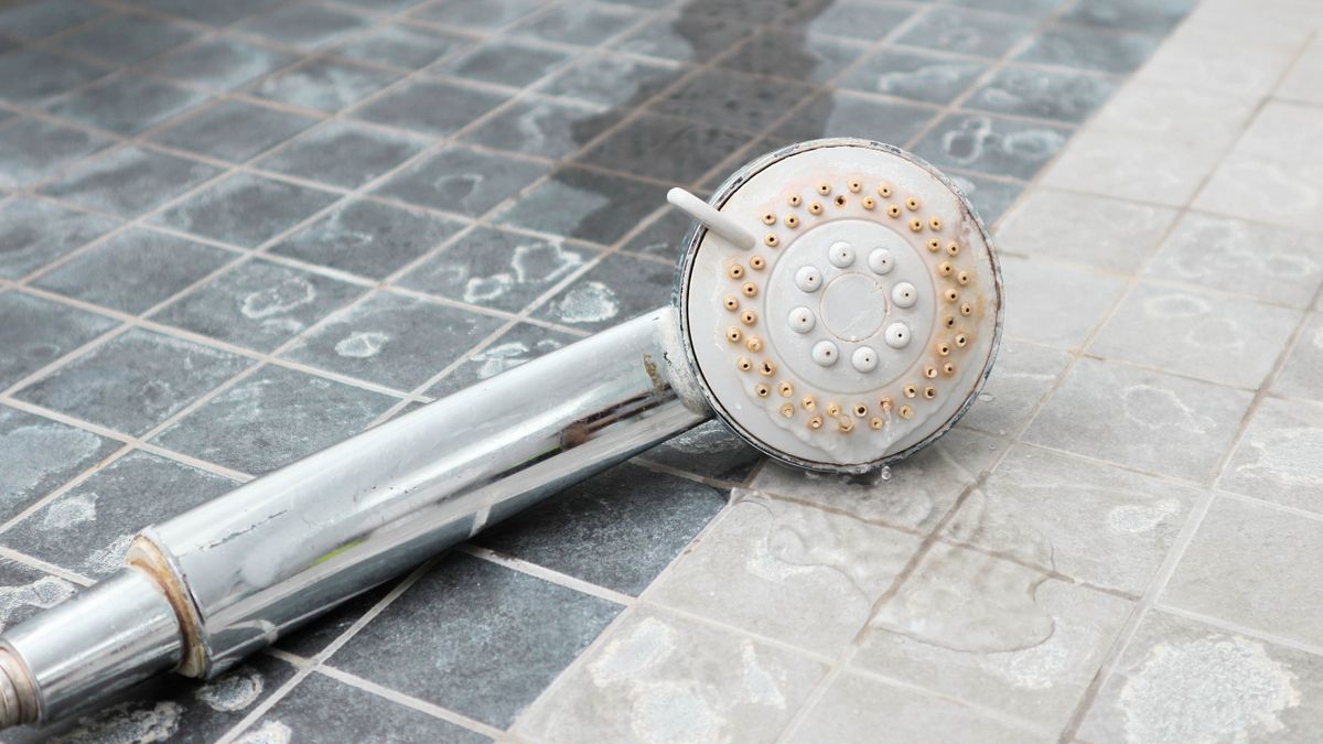 showerhead lying on a bathroom flloor covered in limescale