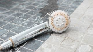 showerhead lying on a bathroom flloor covered in limescale