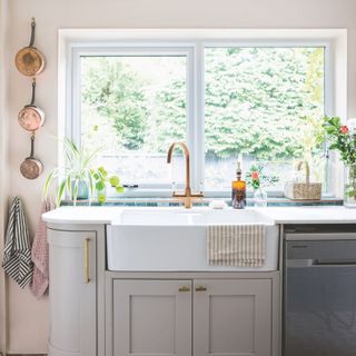 Looking out of a kitchen window with full view of a white sink with grey cabinets and pots on the wall