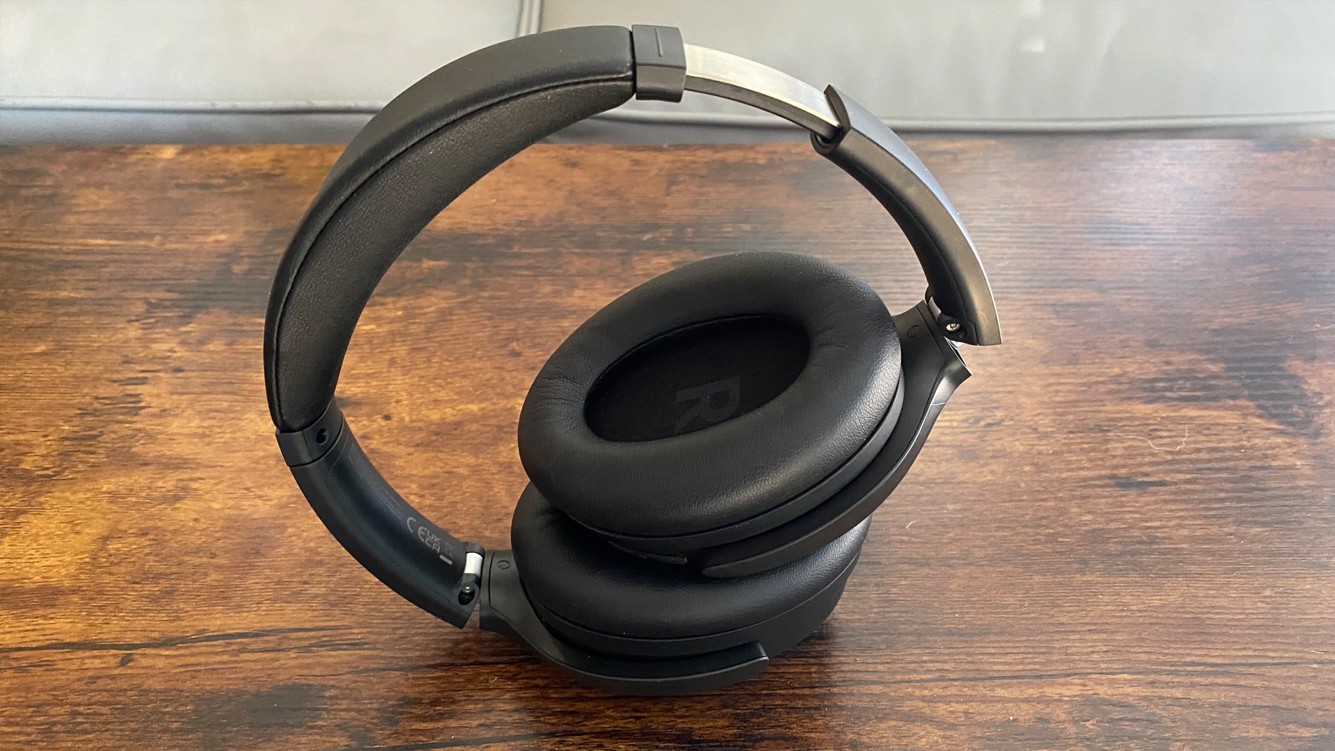 Earfun Wave Life over-ear headphones, with extended headband and folded inwards, on a wooden surface