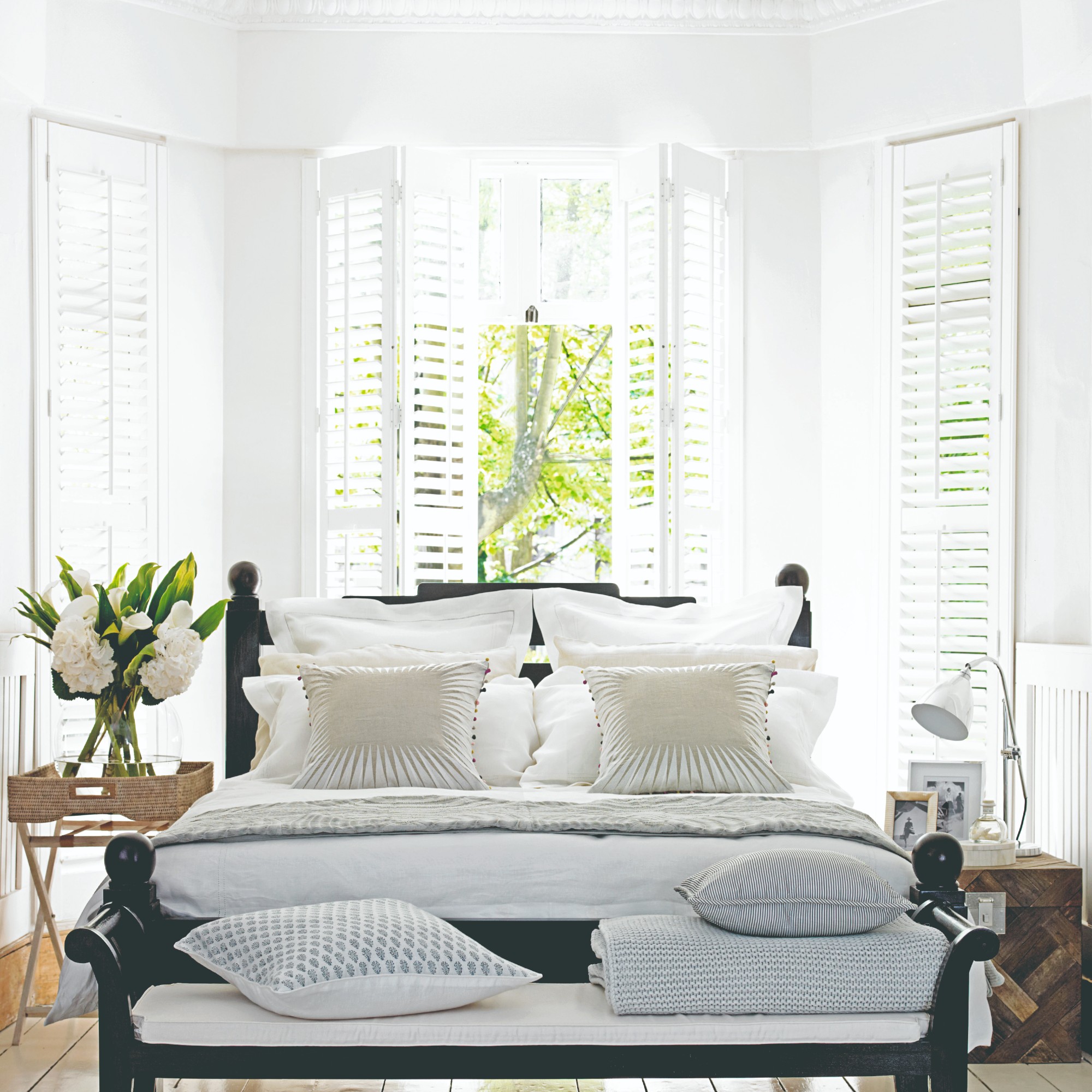 A bedroom with the bed positioned in a bay window with white shutters