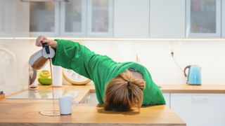 Tired woman is trying to drink coffee, but misses pouring it into her cup and is sleeping with her head on the counter