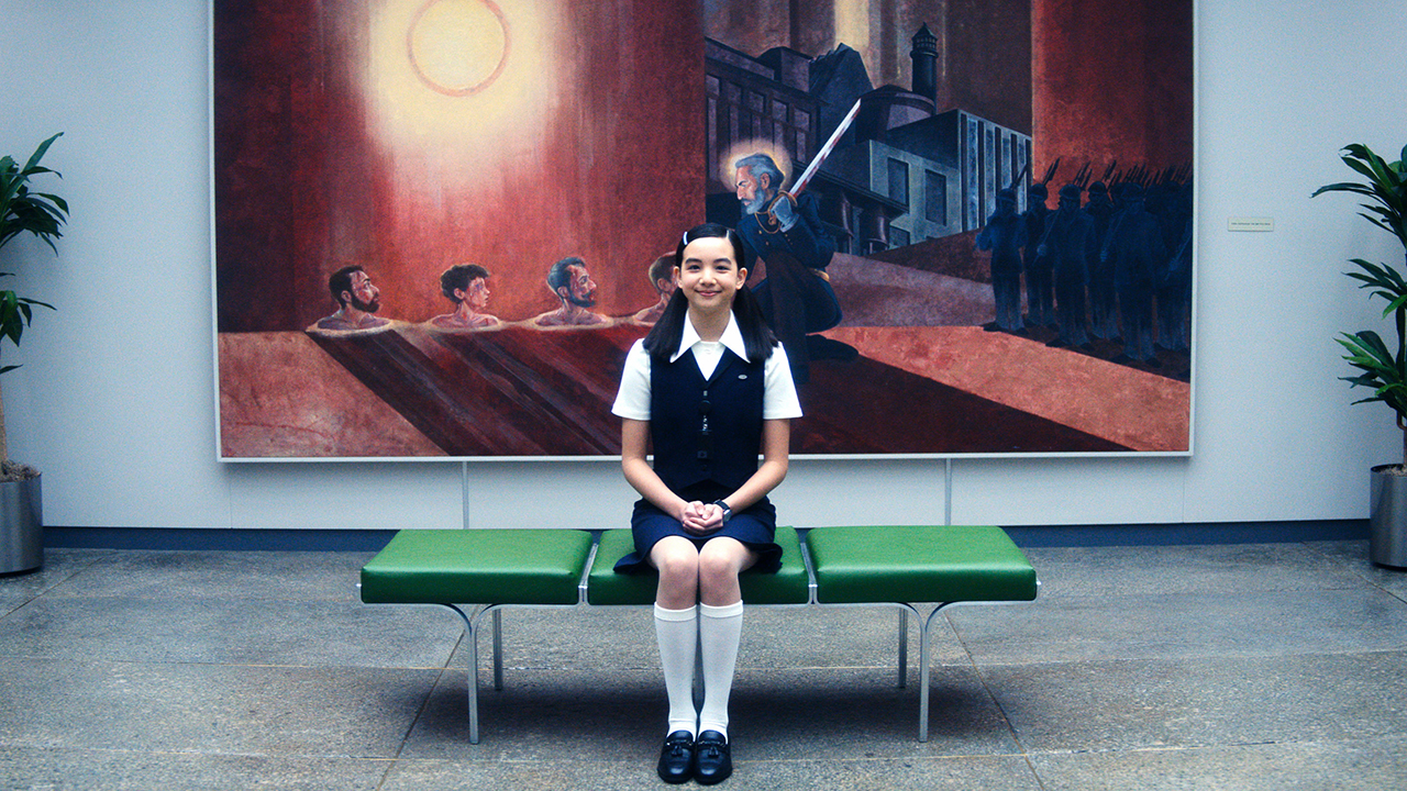 Ms Huang sitting on a bench in front of a painting in Severance season 2 episode 5