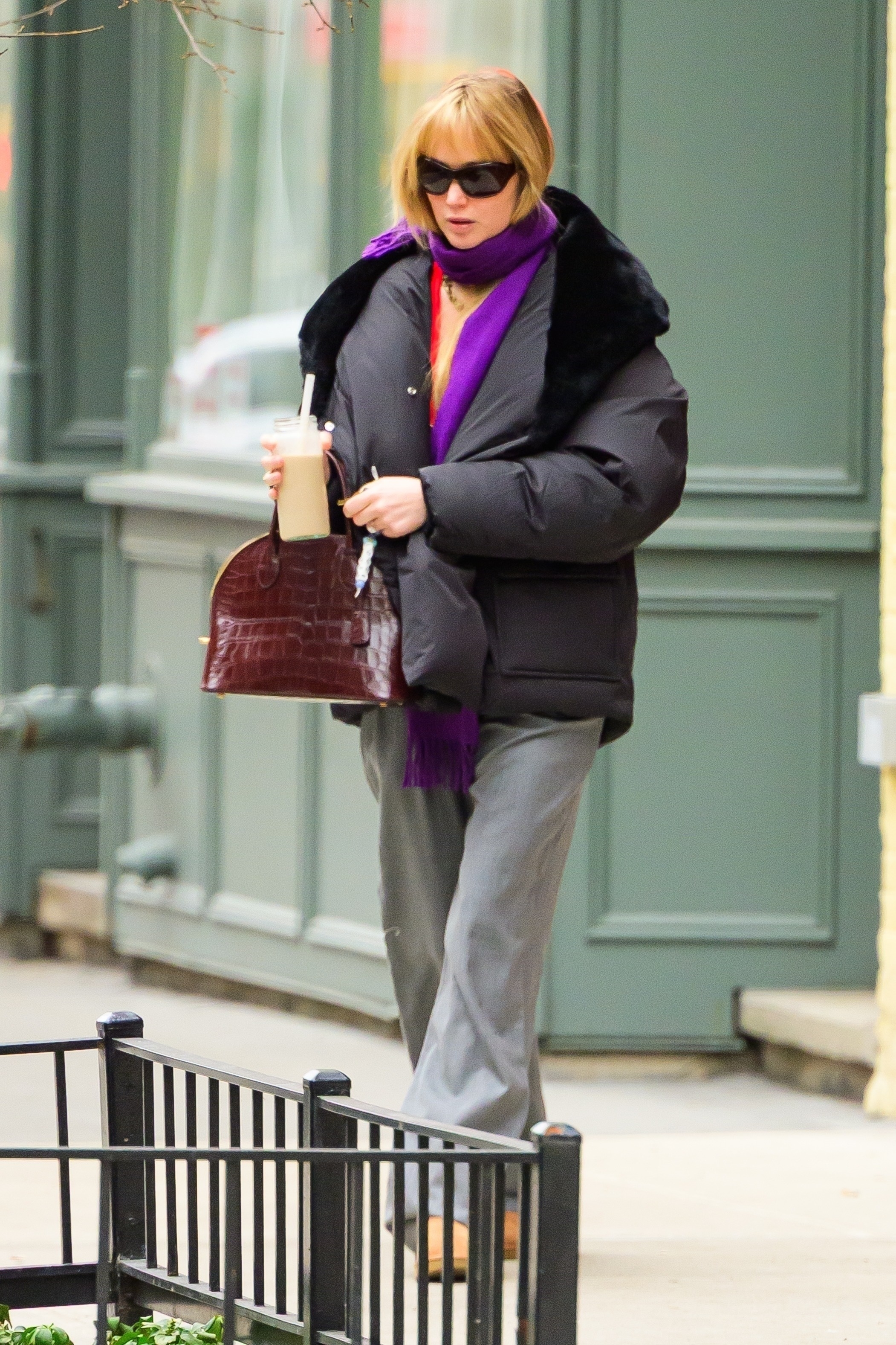 Jennifer Lawrence steps outside in New York wearing a purple scarf with a black puffer jacket and a burgundy crock bag and grey trousers.