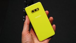 En person, der holder en gul Samsung Galaxy S10e mod en sort baggrund