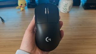 Reviewer hand holding Logitech G Pro X Superlight 2 DEX gaming mouse in black against a PC setup