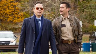 Josh Charles and Josh Segarra walk outside in a Port Wenn park in Season 1 of Best Medicine. It is chilly and both have coats on.