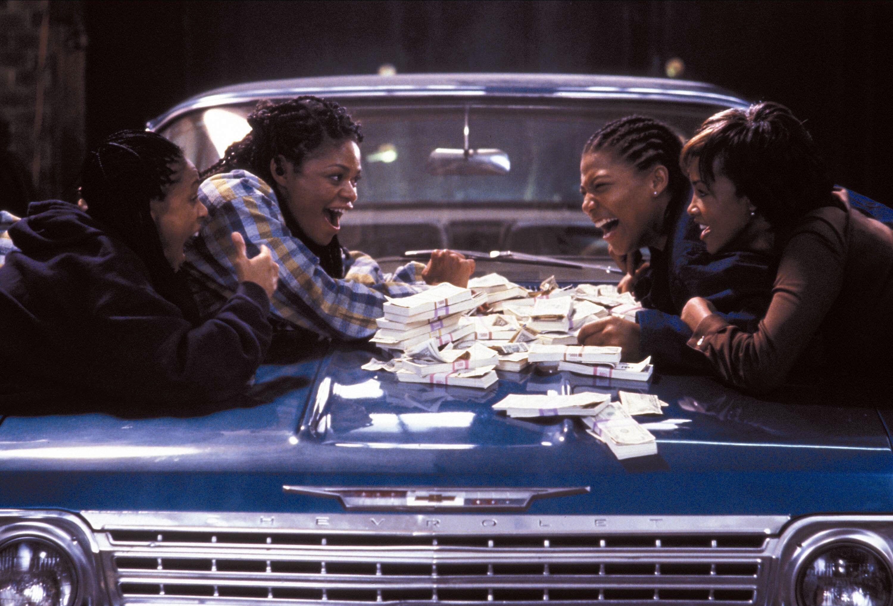 a group of women lean over a car with money on it in a still from the movie set it off