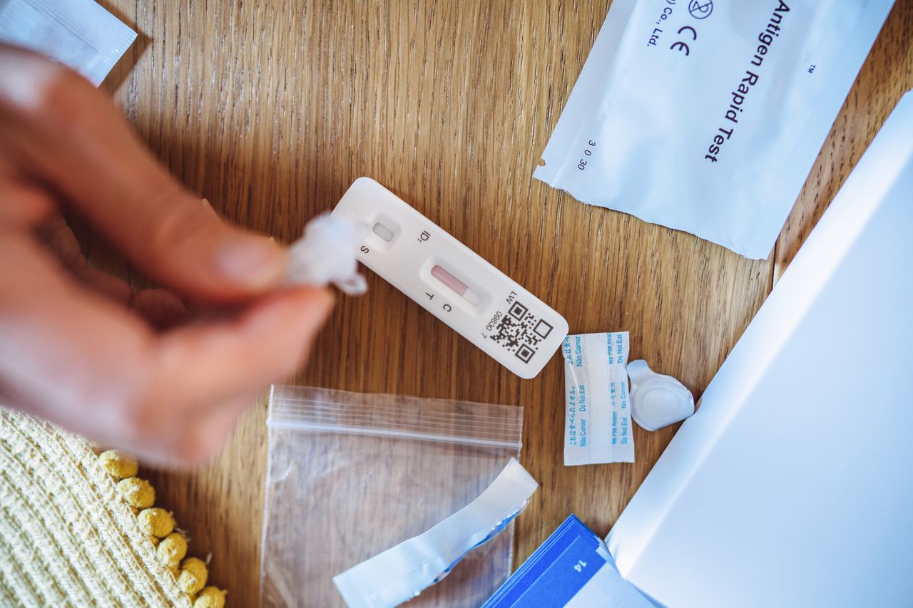 A person holds an at-home COVID-19 test on a desk with supplies from the testing kit. 