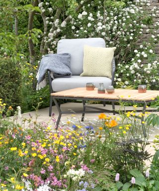 square patio with outdoor armchair and informal planting in flower beds