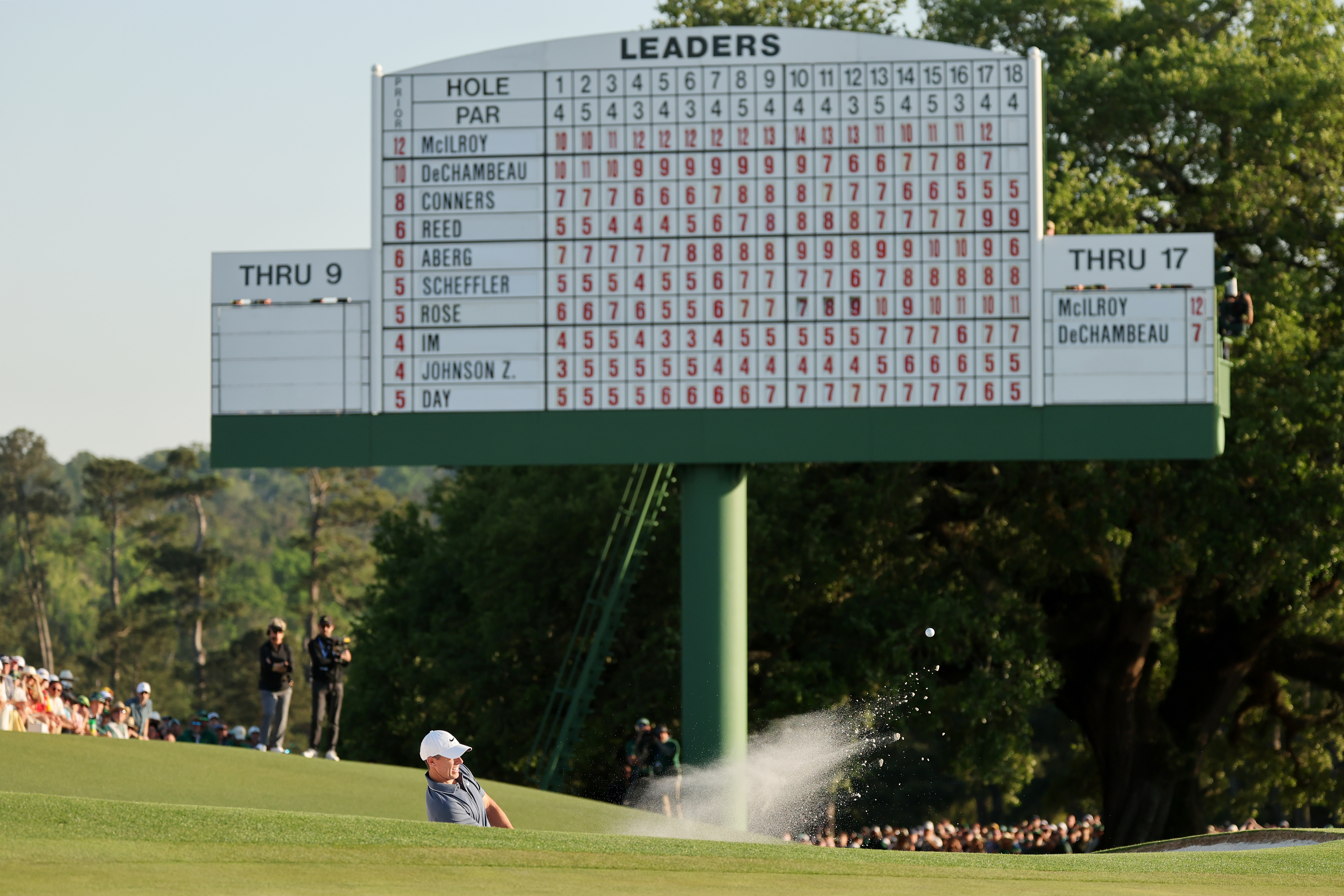 Rory McIlroy hits a bunker shot in front of the big leaderboard on the 18th green at Augusta National during the 2025 Masters
