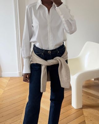 Woman wearing white button down shirt, jeans, and a sweater wrapped around her waist.