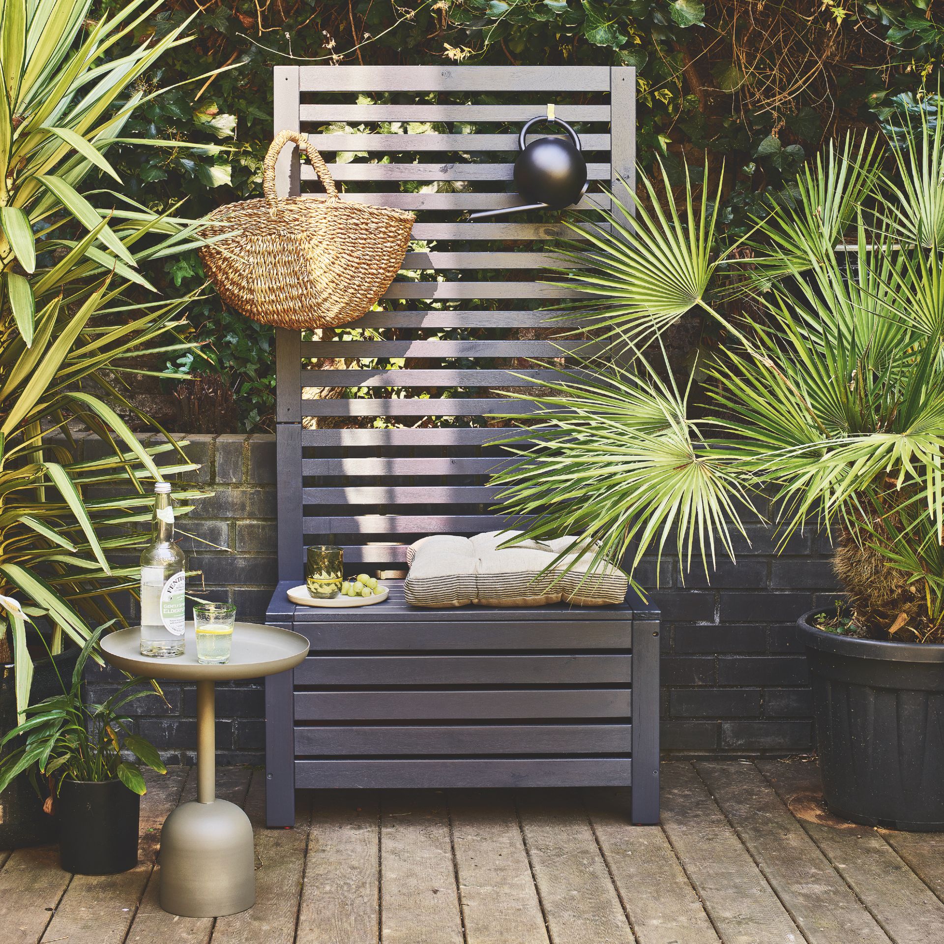 garden with bench seat with high back for hanging and displaying items, plants, side table with drink, seat cushion on bench, basket hanging from top