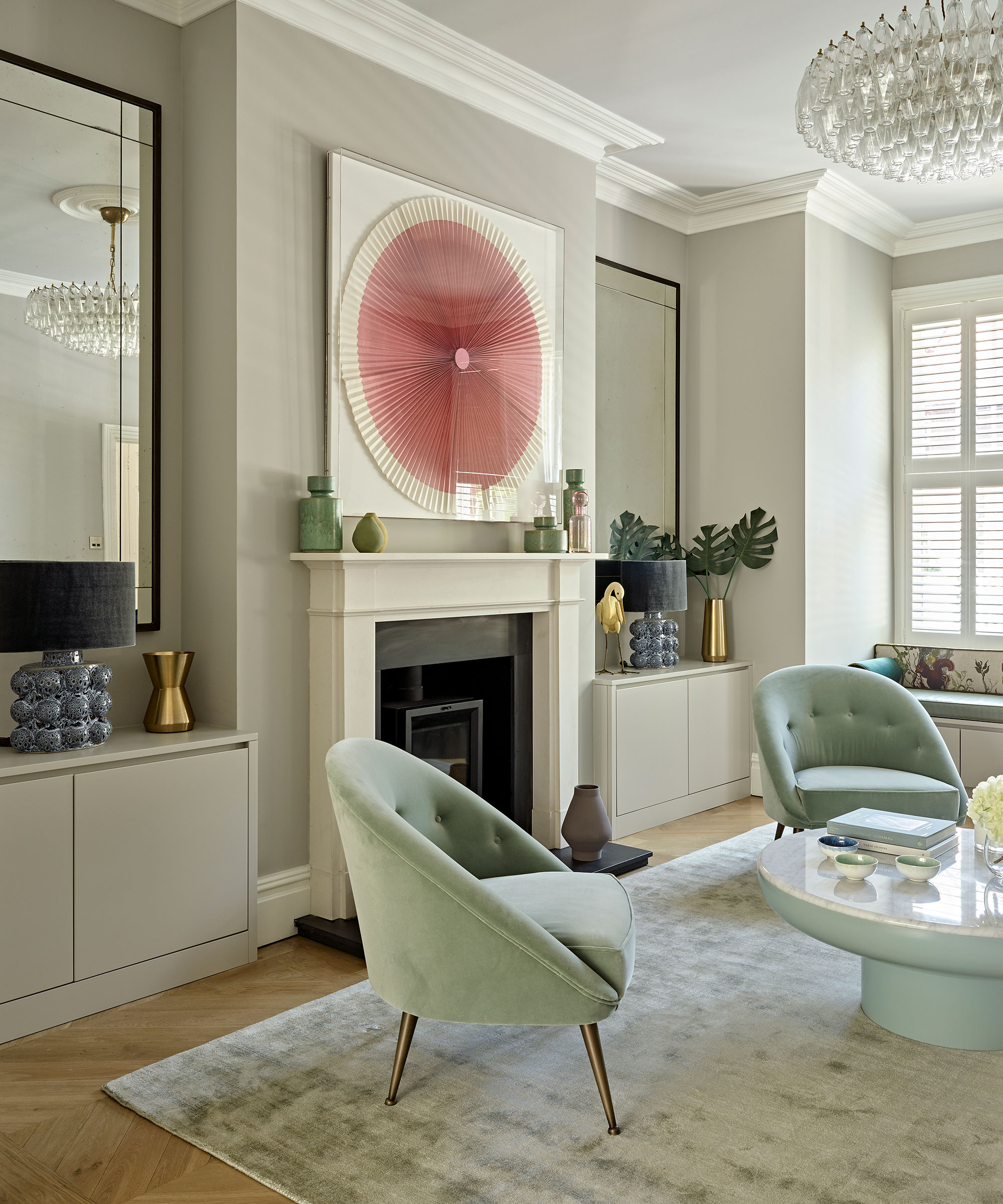 A living room with a large fireplace that has artwork above it and two large mirrors on either side of it.