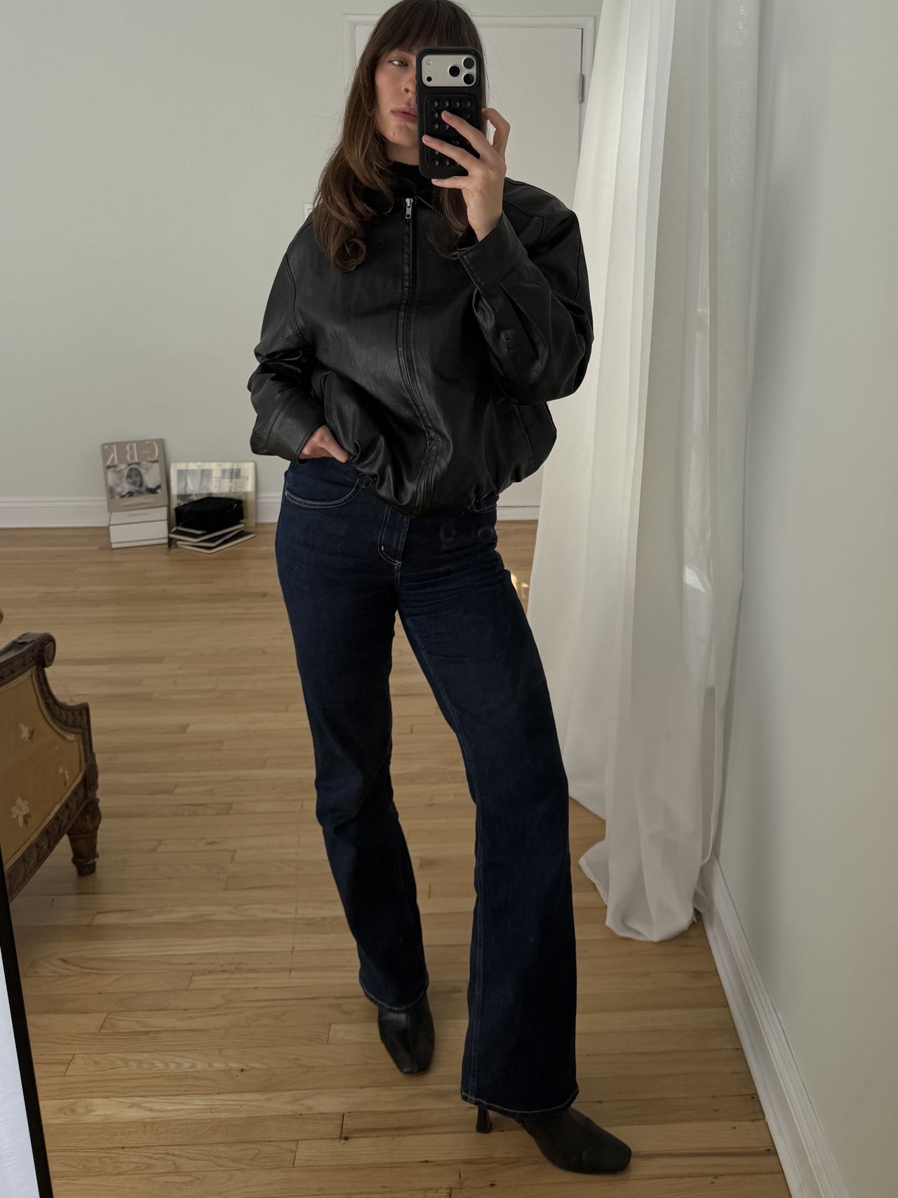Kathryn Zahorak posing in mirror wearing leather jacket, dark wash jeans, and black boots